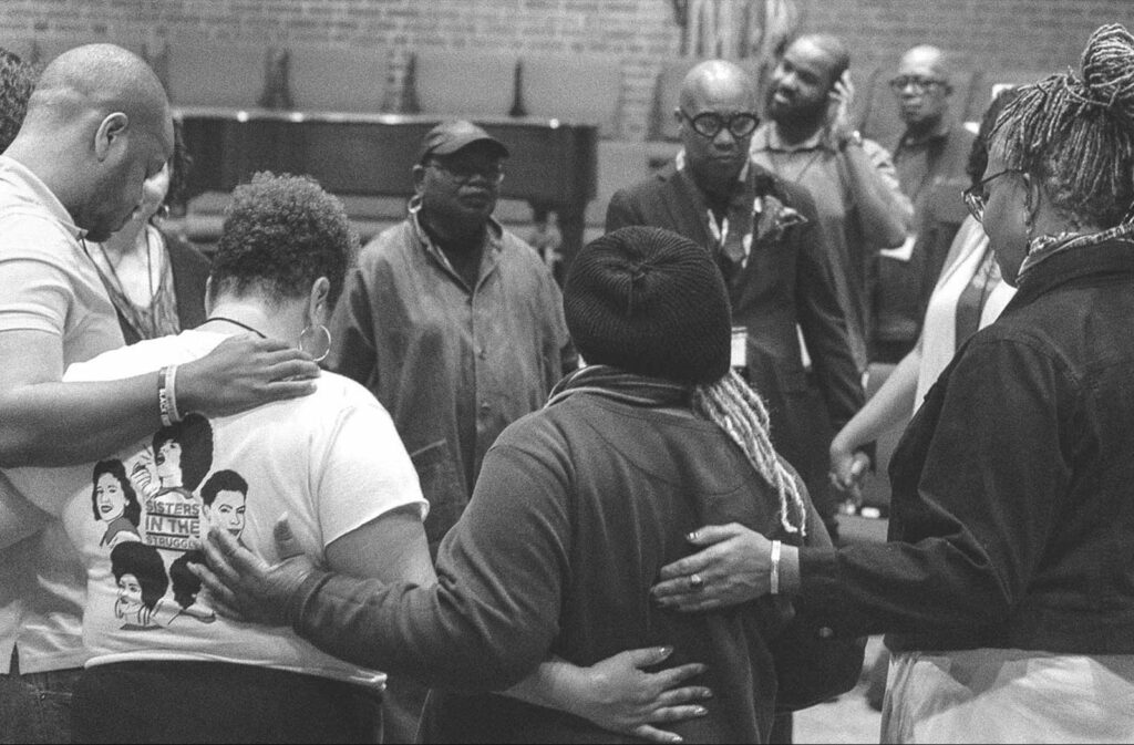 A group of Black people standing in a circle holding hands or touching each other's backs.