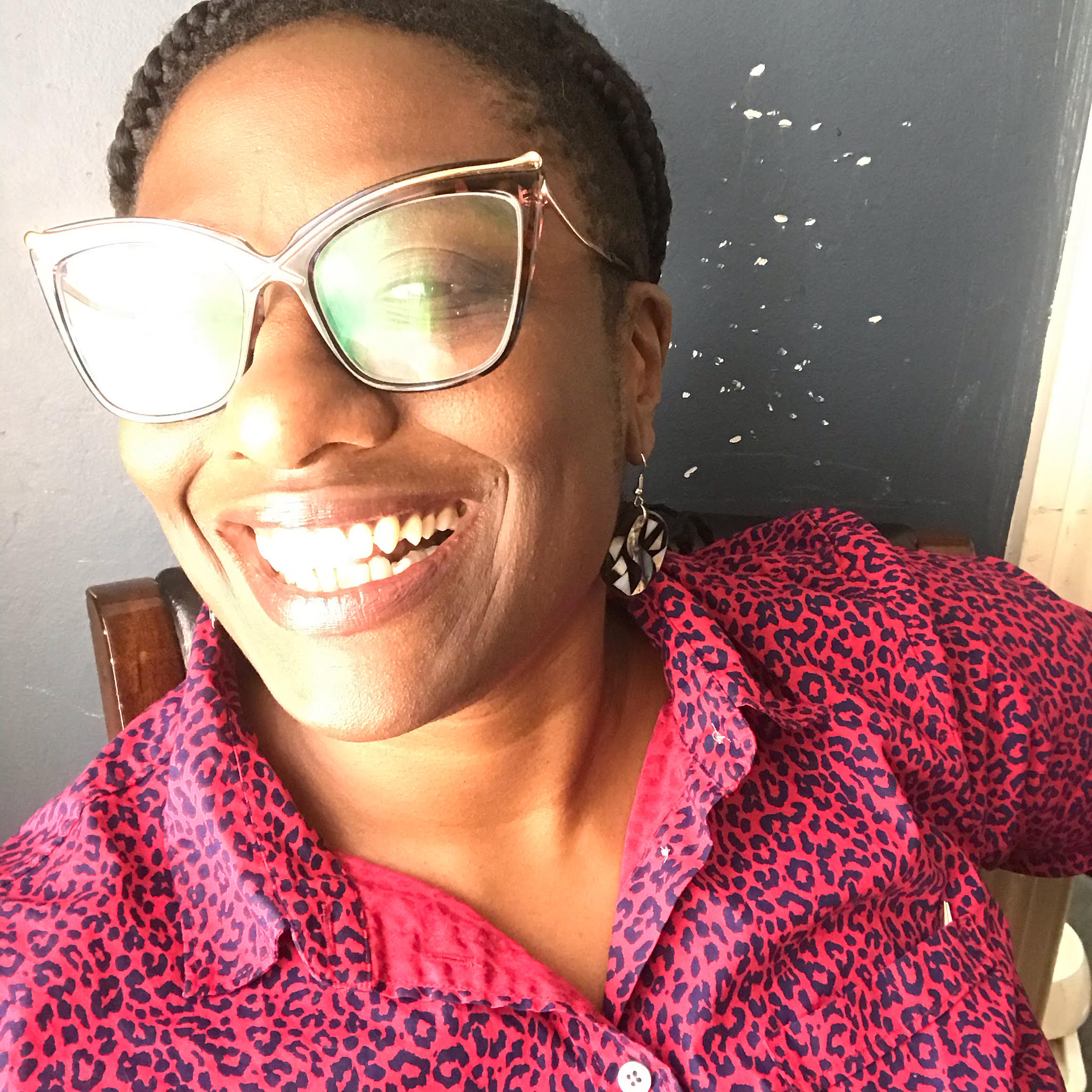 A picture of a Black woman wearing glasses smiling. She is wearing an animal print shirt and earrings.