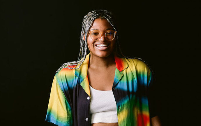 Beatrice Ogeh, a Black person, wears bright clothing while standing in front of a dark background.