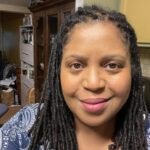 Carla Gates, a Black woman with locs, smiles at the camera.