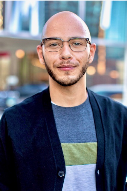 A headshot photo of a Black person with a bold head and glasses